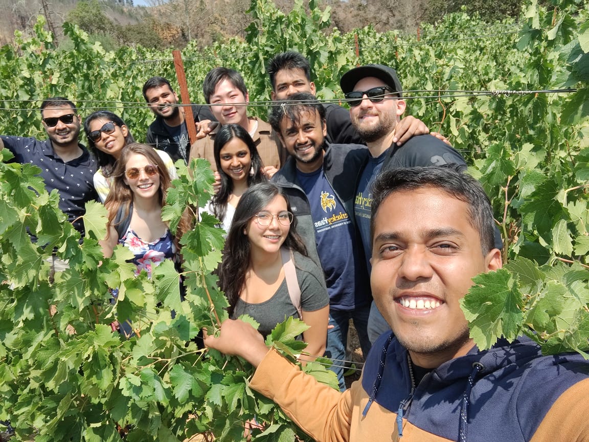 Smiling group of people posing for group selfie amid a vineyard